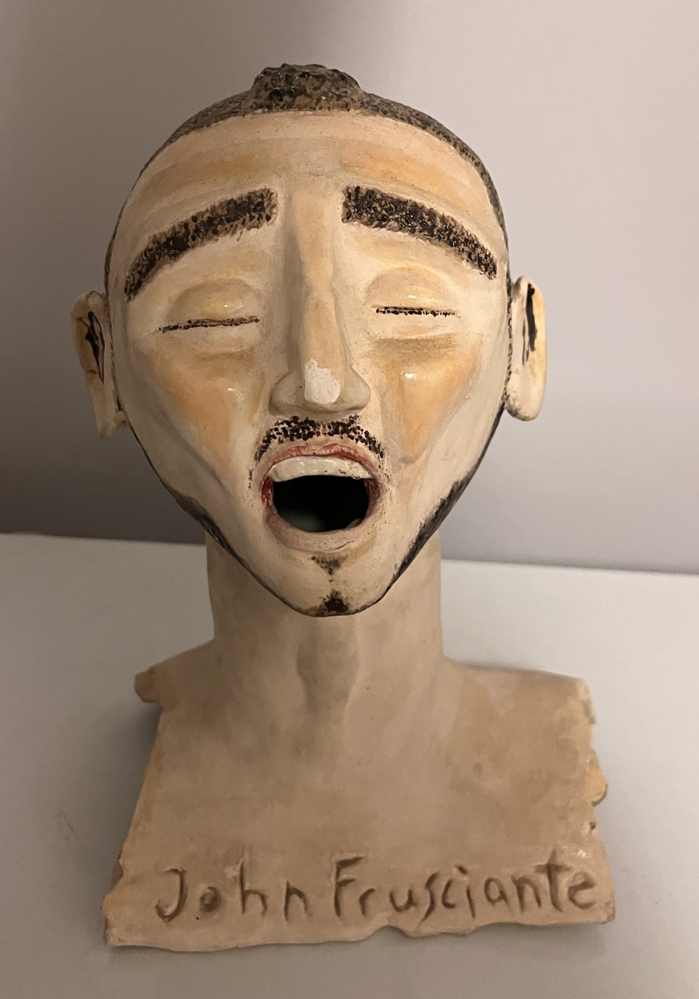 Ceramic bust of John Frusciante singing, mouth open and eyes closed, his name carved into the base