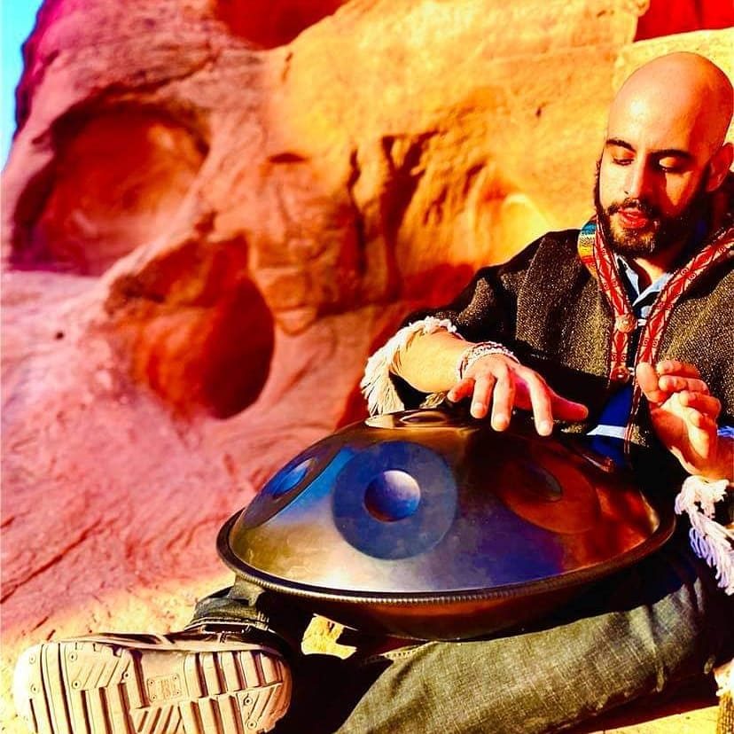 Stefano playing handpan against red sandstone, wearing an Andean textile