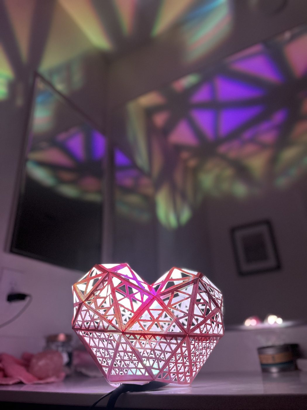 A small cut-paper lattice heart glowing on a counter, throwing colored shadows on the walls