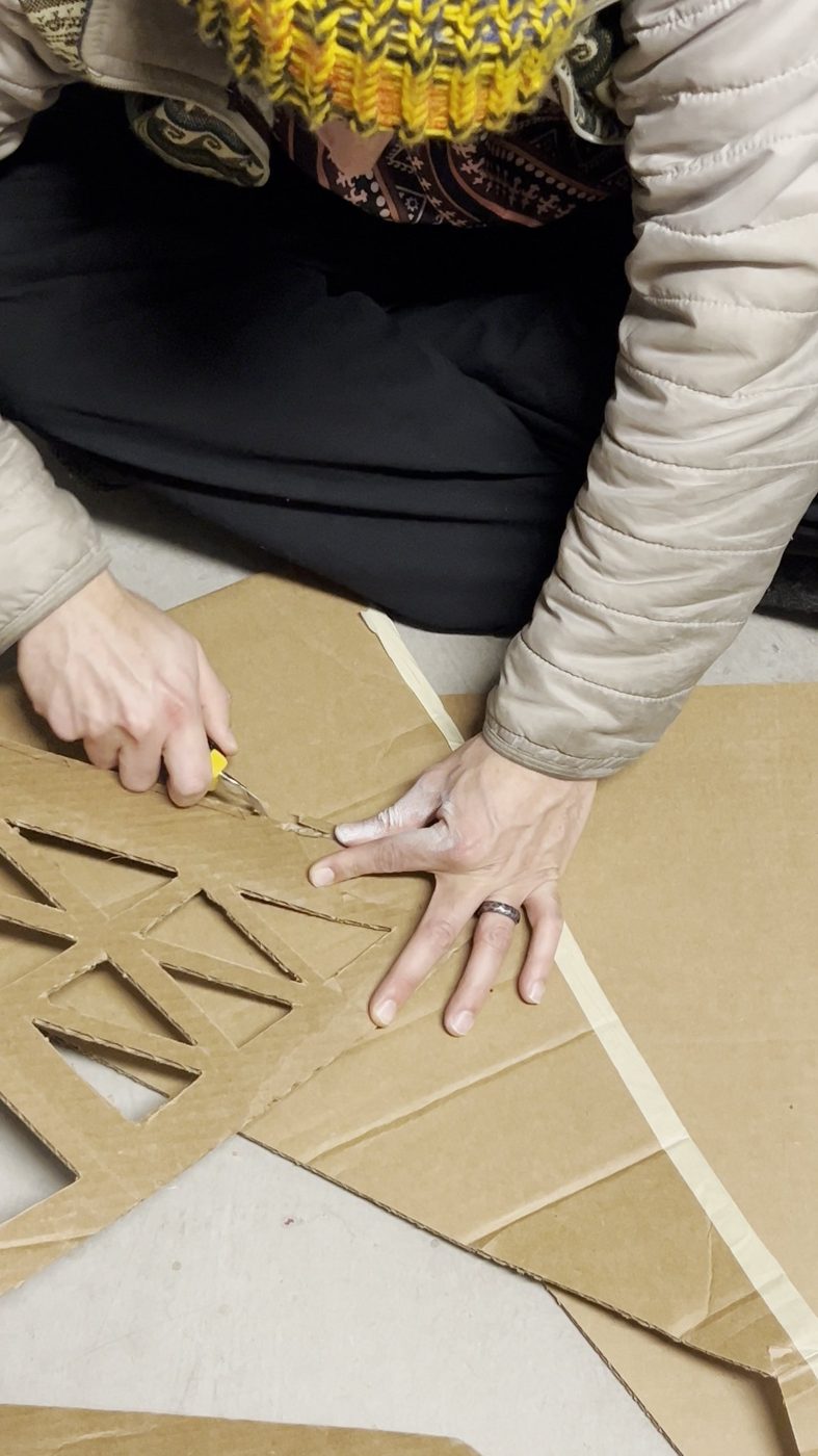 Hands cutting triangular lattice panels from cardboard with a utility knife